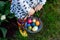 Close-up of legs of toddler girl with colorful stockings and shoes and basket with colored eggs. Child having fun with