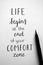 Close-up of `LIFE BEGINS AT THE END OF YOUR COMFORT ZONE` hand-lettered in notebook