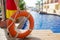 Close up of a lifebuoy ring with rope held up by a lifeguard with a swimming pool on the background . Lifeguard during work