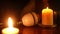 Close-up lightbulb on table with burning candles and blurred woman drinking tea at background. Unrecognizable young lady