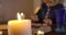 Close-up of lighting candle standing on the table as blurred Caucasian woman taking out cards at the background. Female