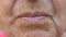 Close up lips of mature grandmother. Mouth of elder grandma sends air kiss into camera. Senior woman with wrinkled skin