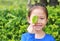 Close up little Asian child girl holding a green leaf closing right eye in green garden background