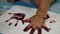 Close up of a little baby girl`s colored hand pressing down on white paper, with help from her mother - baby handprint /