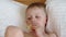 Close-up of a little boy lying on a bed on a white pillow and eating an apple.