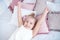 Close-up little girl waking up with stretching arms while awake lying on white bed linen