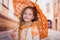 Close up of little girl wearing a beautiful colonial costume and holding an orange umbrella in a blurred background