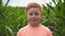 Close up of little smiling red-haired boy with freckles looking into camera against the background of corn field at