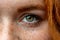 Close up macro face of young red ginger freckled woman with beautiful green eyes