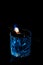 Close up, macro. A glass of blue alcohol, on it lies a fork with a piece of sugar. Sugar is consumed by fire and caramelized.