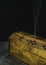 A close up macro photograph of a long wooden incense burner holder on a grey stone tile base with black background and copy space