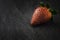 A close up macro photograph of a whole fresh ripe organic strawberry on a dark black slate stone background