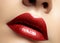Close-up macro shot of female mouth. Glamour red lips Makeup with sensuality gesture. Metalic gloss lipstick