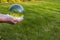 Close up macro view of hand holding crystal ball with inverted image of green natural landscape