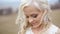 Close up of magical beautiful young blonde bride softly touching her face. Outdoor blurred background