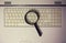 Close up of a magnifying glass on an old laptop keyboard. Computer search engine. Browsing network for answer to every question.