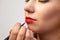 Close-up of make-up applying on the model`s lips, the make-up artist holds a brush in her hand and applies red lipstick, the