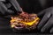 Close-up, making grilled burger. Chef hands in black gloves are puts slice of bacon in burger