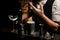 Close-up male bartender pours drink from metal jigger into smoky steel cup of shaker