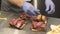 Close-up of male chef hands in gloves preparing delicious sandwiches with pastrami and pickles in the kitchen