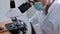 Close-up of a male doctor in uniform examines a biomaterial under a microscope while sitting in a medical laboratory. A medic exam