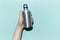 Close-up of male hand holding eco, reusable aluminum thermo water bottle on studio background of cyan, aqua menthe color.