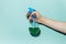 Close-up of male hand holding spray bottle for cleaning with blue pump, on cyan background.