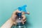 Close-up of male hand holding spray bottle for cleaning with blue pump, on cyan background.