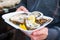 Close up male hand holding take away food tray with fresh opened oyster and lemon slices at street food market, festival, event. S