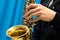 Close-up of a male hand playing a musician on a gold saxophone on a blue background. Theme for music news.