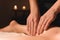 Close-up of male hands doing calf massage of female legs in a dark room with candles in the background. Cosmetology and