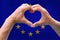 Close-up of male hands in heart form against background of silk national flag of European state of Spain, patriots of country