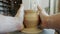 Close-up of male hands making ceramic pot from wet clay on throwing wheel