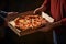 Close-up of male hands taking pizza from cardboard box on dark background, Man delivery pizza to a customer, top section cropped,