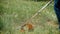 Close up male worker keeping electric trimmer and cutting grass in slow motion