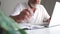 Close-up a man with a beard with glasses and a white T-shirt takes notes in his notebook and works with a laptop