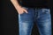 Close up of a man in classic blue jeans trousers with a hand in the pocket and black shirt against black background. Male casual