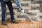 Close up of a man cleaning terrace with a power washer - high water pressure cleaner on wooden terrace surface