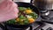 Close-up of man cooking fried eggs with chopped spinach and sun-dried tomatoes in black cast-iron frying pan, selective focus