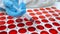 Close up of man hand with blue glove holding a syringe taking a sample of red liquid from a group of round red clinical samples