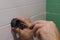 Close-up of man hands attaching plastic component of shower head holder to tiled wall screwing in nail with screwdriver