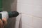 Close-up of man hands with drill making holes for dowels into tiled wall in washroom causing loud noise. Renovation