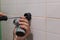 Close-up of man hands installing shower head holder with screwdriver to tiled wall in washroom during renovation works