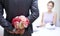 Close up of man hiding flowers behind from woman