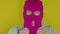Close up of man puts on pink balaclava on yellow background. Secretive guy puts on mask, looking at camera.