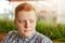 A close-up of a man with round face having red hair and freckles dressed in checked shirt having pensive expression looking aside