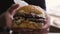 Close-up of a man`s hand holding a big mouth-watering juicy Burger.