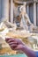 Close up of a man`s hand holding a coin in front of Fountain Di Trevi in Rome, Italy.