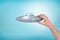 Close-up of man`s hand holding small light-gray UFO on light-blue background.