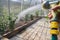 A close-up of a man& x27;s hand under pressure sprays an aqueous solution on a flower bed with plants in a greenhouse